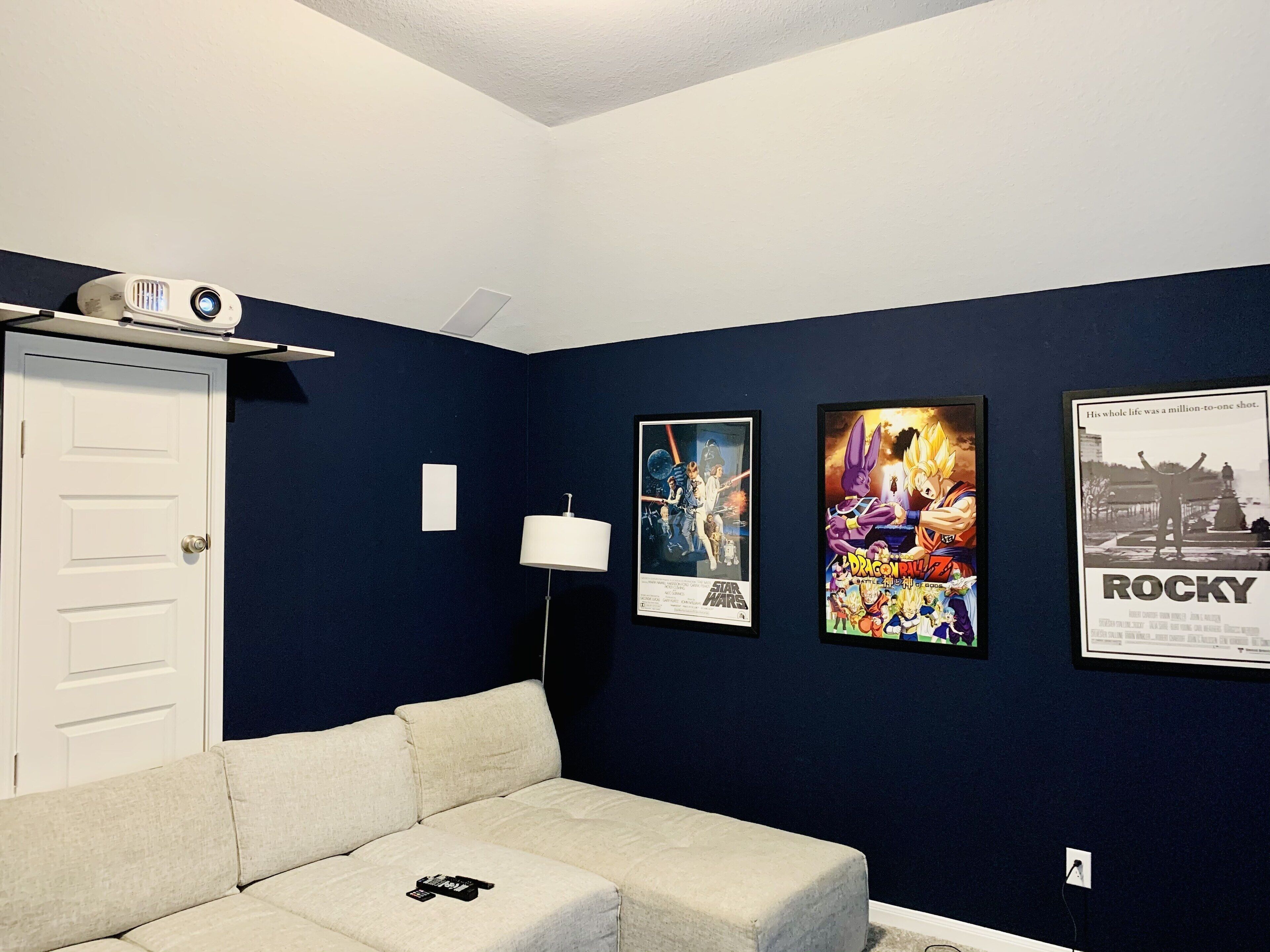 Ein Zimmer mit dunkelblauer Wand, einer weißen Tür, einem weißen Sofa und drei Bildern an der Wand.