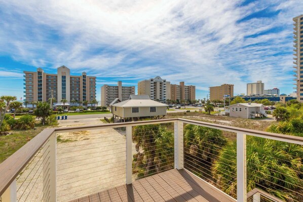 Una propiedad frente a la playa con una terraza de madera, un edificio pequeño y varios hoteles altos al fondo.