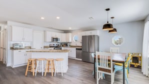 A modern kitchen with white cabinets, a central island with stools, stainless steel appliances, and pendant lighting. - Sel De Vie A 4 Bedrooms Sleeps 10 (Gulf Shores)