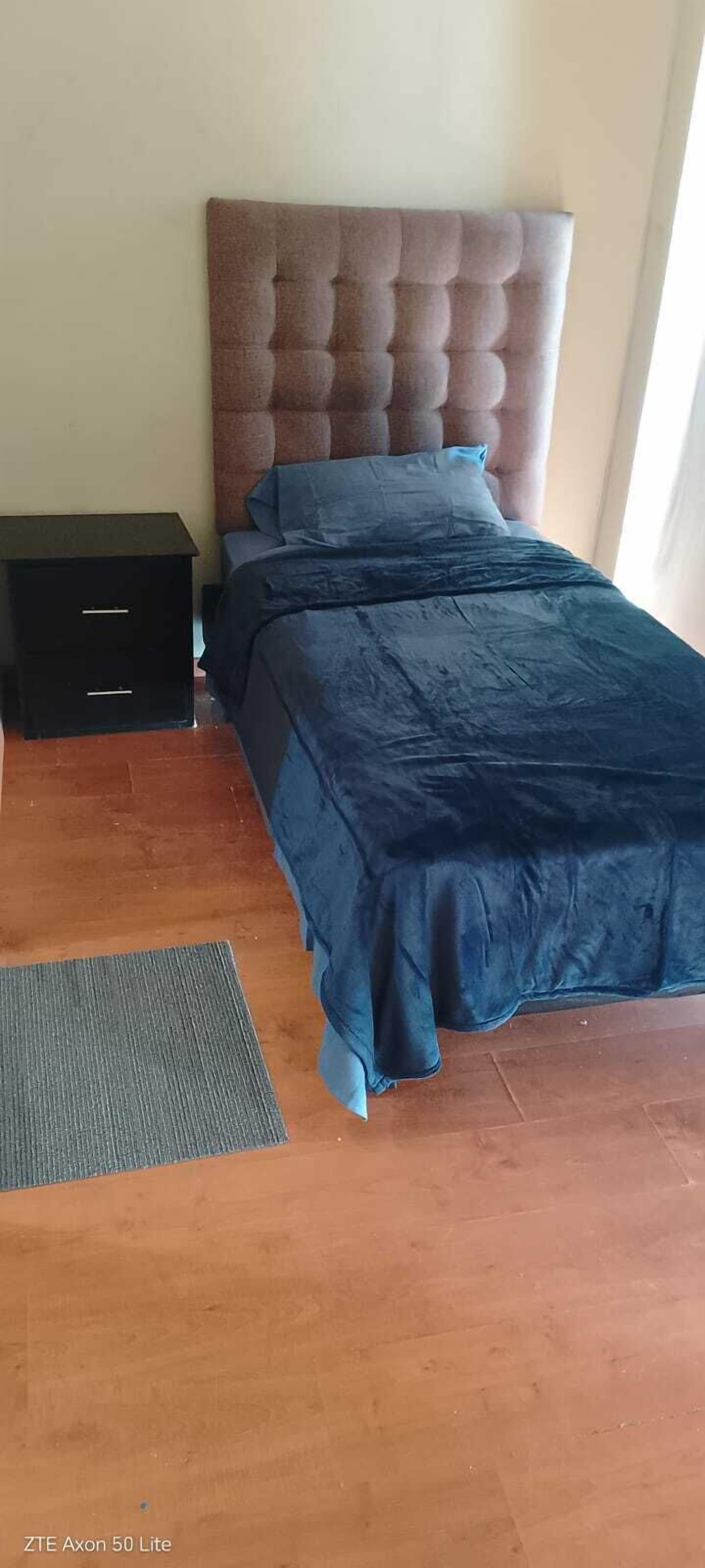 A bedroom with a tufted headboard, a bed with dark blue bedding, a small black nightstand, and a grey rug on a wooden floor.