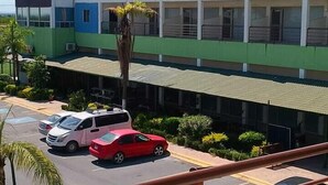 A parking area with several cars, a building with multiple windows, and a clear sky. - HOTEL KOREA GARDEN (Apodaca)