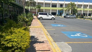 A parking lot with a white van and a silver car, a building with a green roof, and a clear blue sky. - HOTEL KOREA GARDEN (Apodaca)