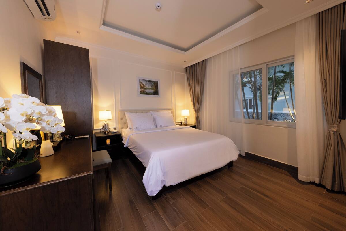 A hotel room with a large bed, bedside lamps, a nightstand, a mirror, and a window with curtains.
