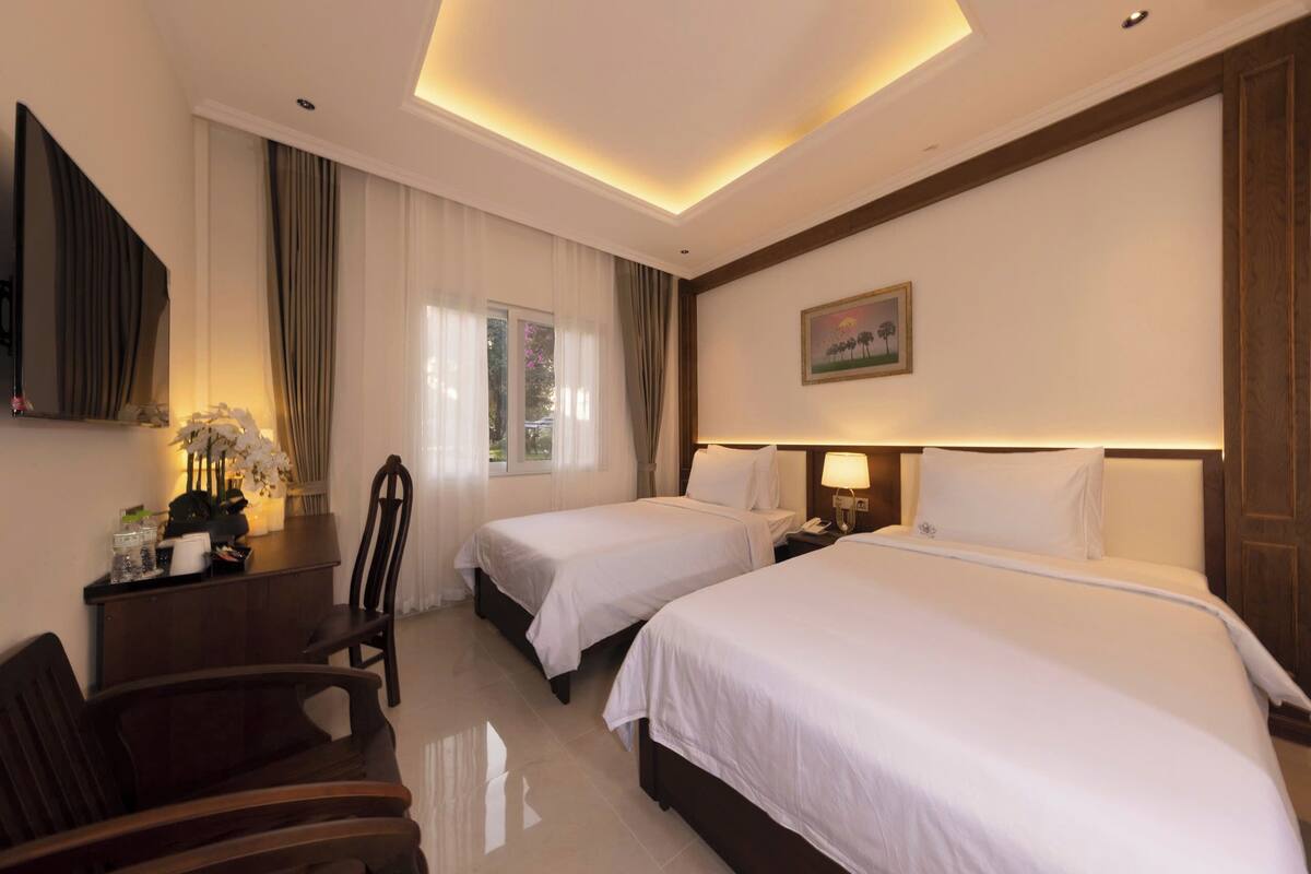 A hotel room with two beds, a desk with a chair, a TV, and a painting on the wall.