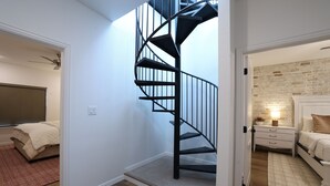 Ein Schlafzimmer mit modernem Design, das eine Wendeltreppe, eine Ziegelwand als Blickfang und ein großes Bett mit Nachttisch zeigt.
