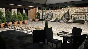 An outdoor patio area with round tables and chairs, surrounded by potted plants and a stone wall. - Hotel bani (Kutaisi)