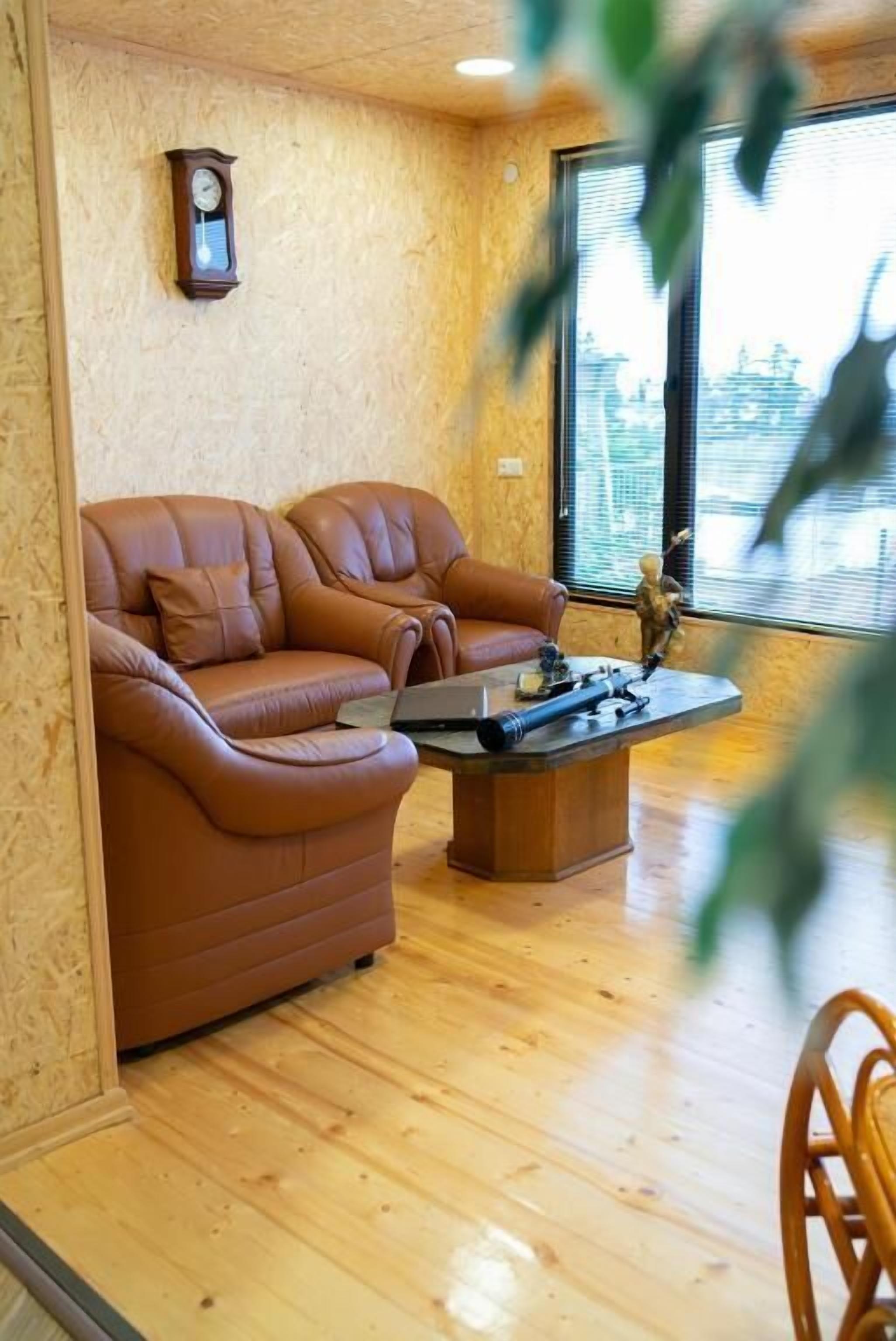Una habitación acogedora con un sofá de cuero marrón, una mesa de centro de madera y un reloj en la pared.