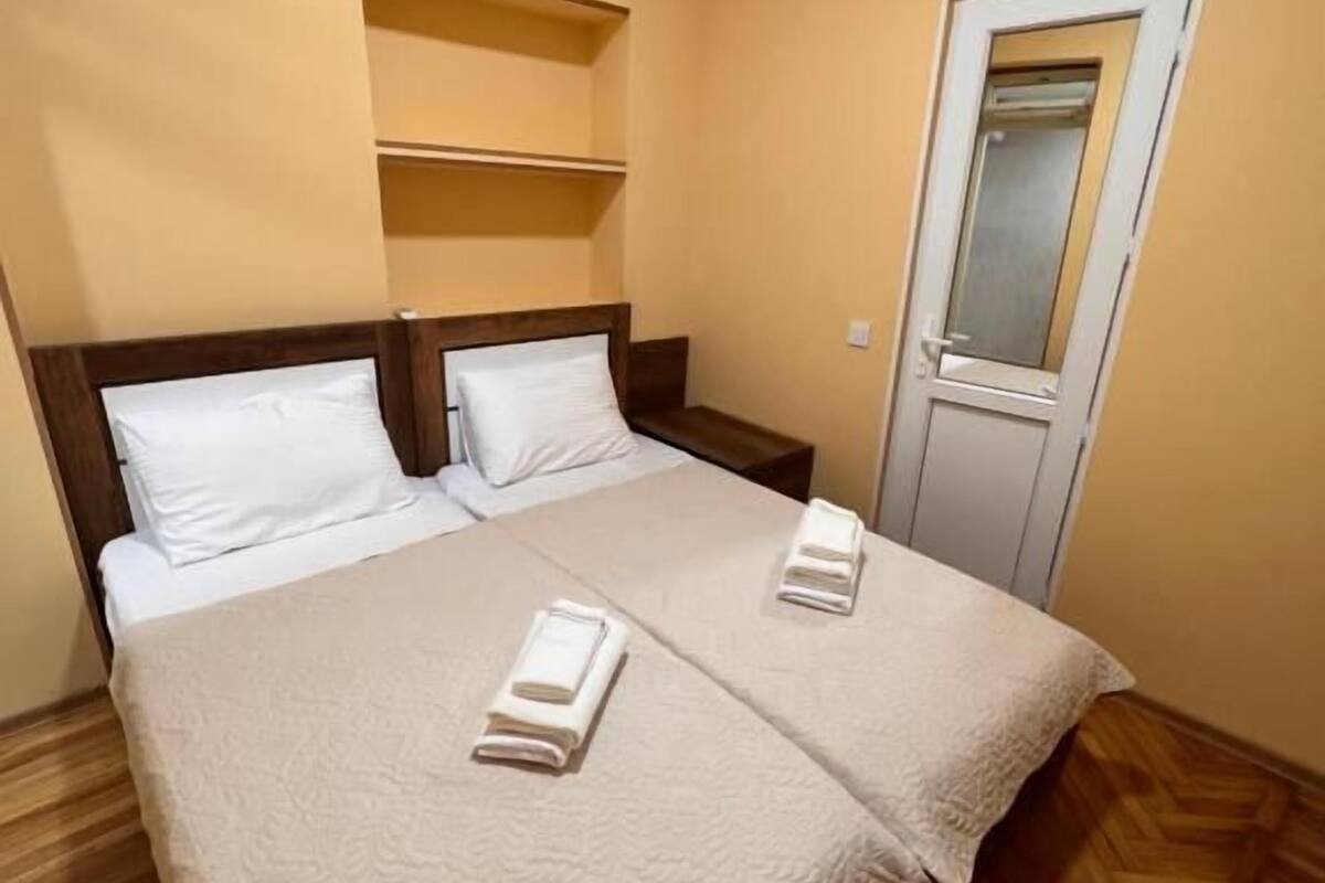 Habitación de hotel con una cama, dos almohadas, una mesita de noche, un espejo y un equipo de aire acondicionado.