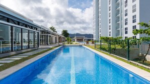 A swimming pool with a clear blue water surface, surrounded by a modern building with large windows and a glass facade. - Casago | Beach & Marine Design Condo in Jacó (Jaco)