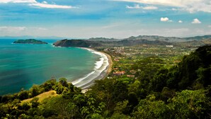 A coastal landscape with a beach, buildings, and greenery. - Casago | Beach & Marine Design Condo in Jacó (Jaco)
