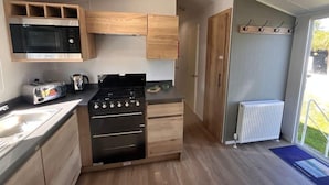 Et kompakt køkken med træskabe, indbygget mikroovn, gasblus og en lille bordplade.