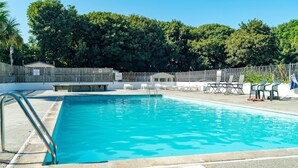 En swimmingpool med en metalstige, omgivet af liggestole og et træhegn.