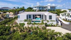 A modern house with a swimming pool, surrounded by lush greenery and palm trees. - Villa Pluto · Award-Winning · Private · Concierge (Providenciales)
