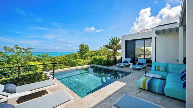 A modern outdoor pool area with lounge chairs and a sofa, overlooking a scenic ocean view. - Villa Pluto · Award-Winning · Private · Concierge (Providenciales)