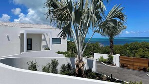 A modern house with a white exterior, a curved driveway, and a view of the ocean. - Villa Pluto · Award-Winning · Private · Concierge (Providenciales)