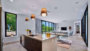 A modern kitchen with a large island, pendant lights, and a view of greenery outside. - Villa Pluto · Award-Winning · Private · Concierge (Providenciales)