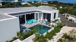 A modern house with a swimming pool, a covered outdoor seating area, and a view of the surrounding landscape. - Villa Pluto · Award-Winning · Private · Concierge (Providenciales)