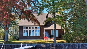 A cabin with a dock extending into a body of water, surrounded by trees with autumn foliage. - Spacious 4-bedroom lakefront house with WiFi, AC in tranquil Houghton Lake (Houghton Lake)