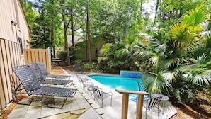 Un espace aménagé au bord de la piscine, avec des chaises longues et une petite table, entouré de plantes et d’arbres tropicaux.