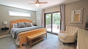 Une chambre à coucher comprenant un lit, des tables de chevet, une chaise, un ventilateur de plafond et une grande fenêtre.