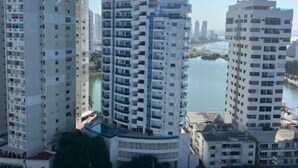 A high-rise residential building with multiple balconies, a river in the background, and a clear sky.