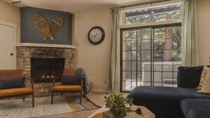 A living room with a stone fireplace, two sofas, a coffee table, and a large window with a view of trees. - The Incline Cabin, Hot Tub | Fireplace | Arcade | 5min to Diamond Pk (Incline Village)