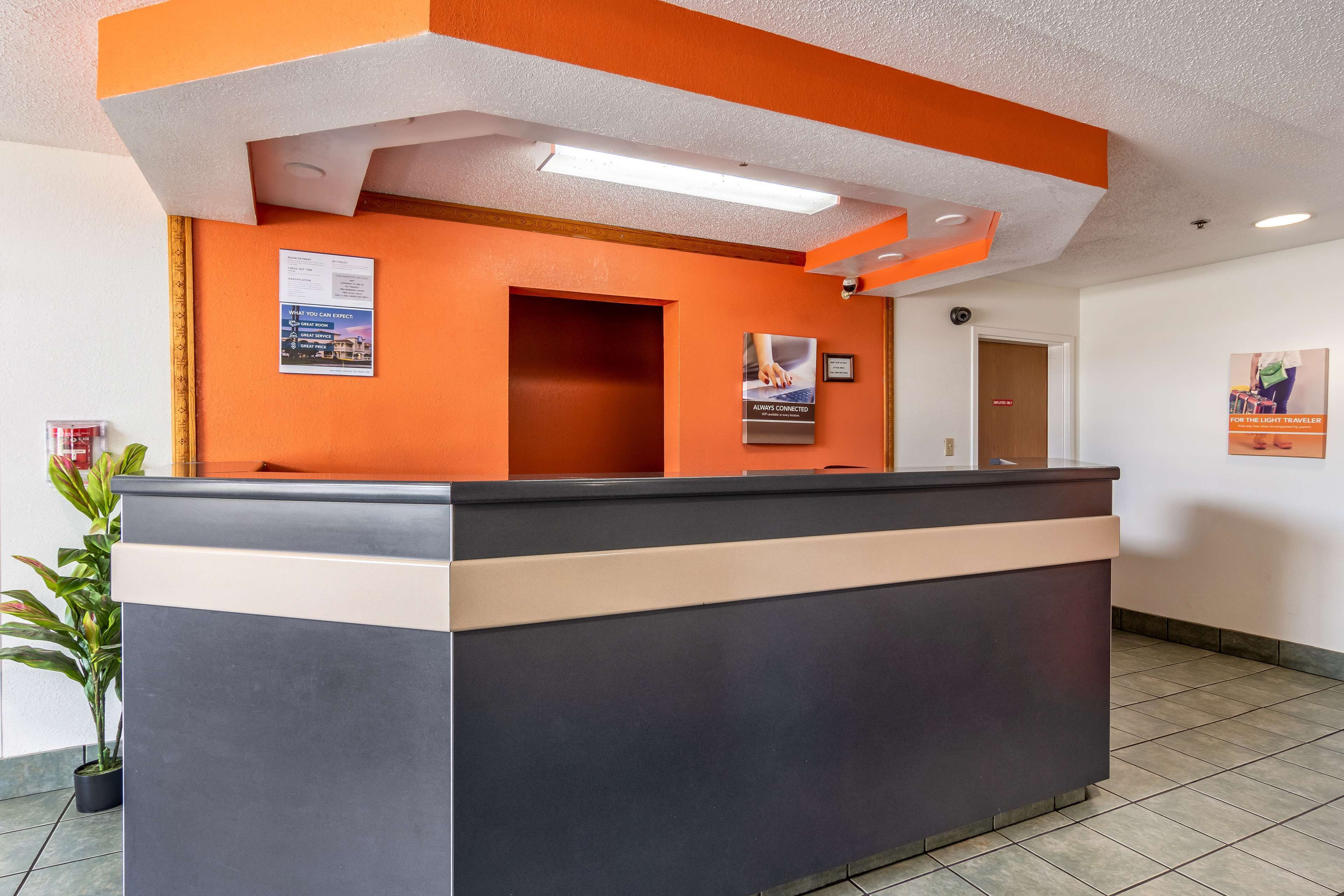 A reception desk with a black and orange color scheme, a potted plant to the left, and a door leading to another room.