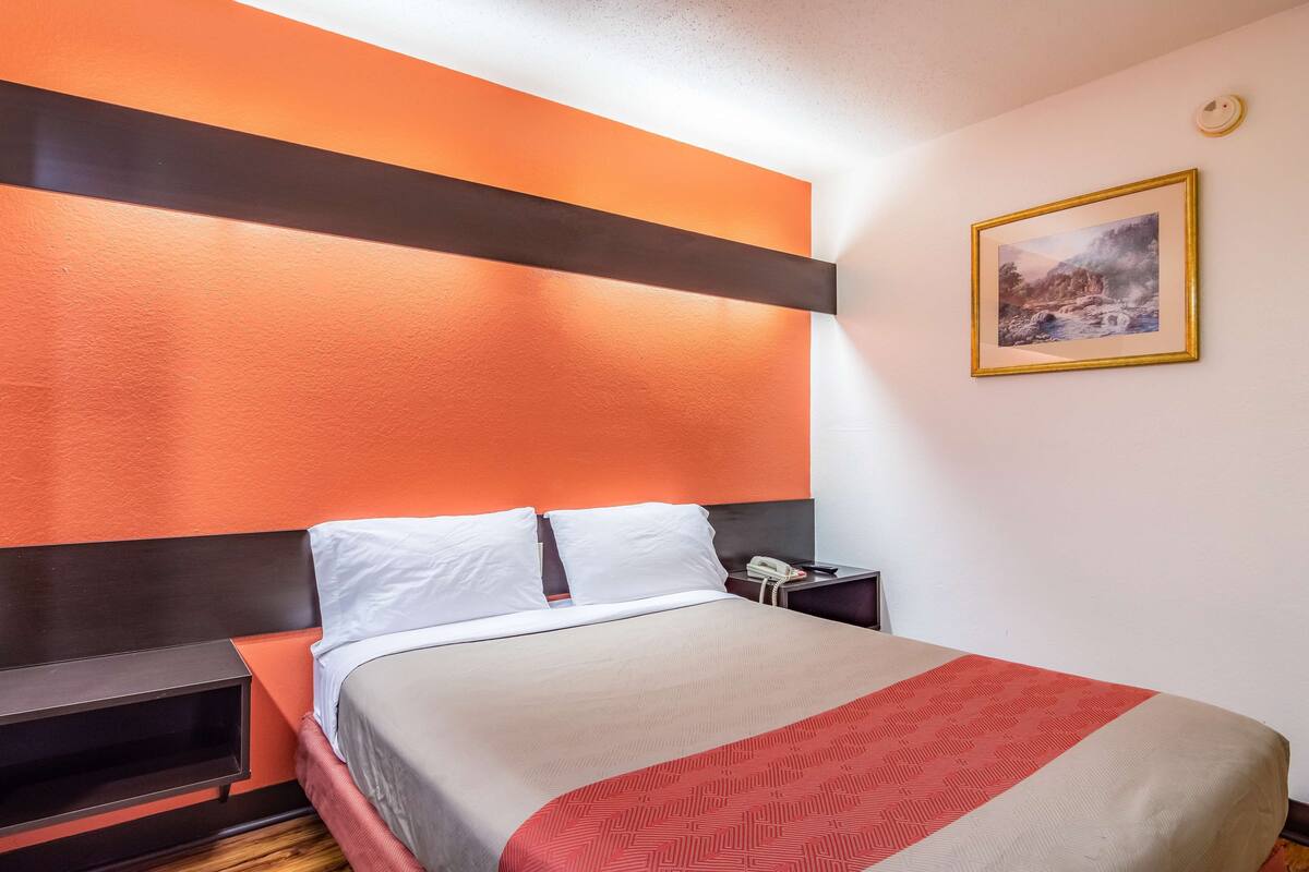 Une chambre d’hôtel avec un lit, une table de chevet, un téléphone et un tableau accroché au mur.