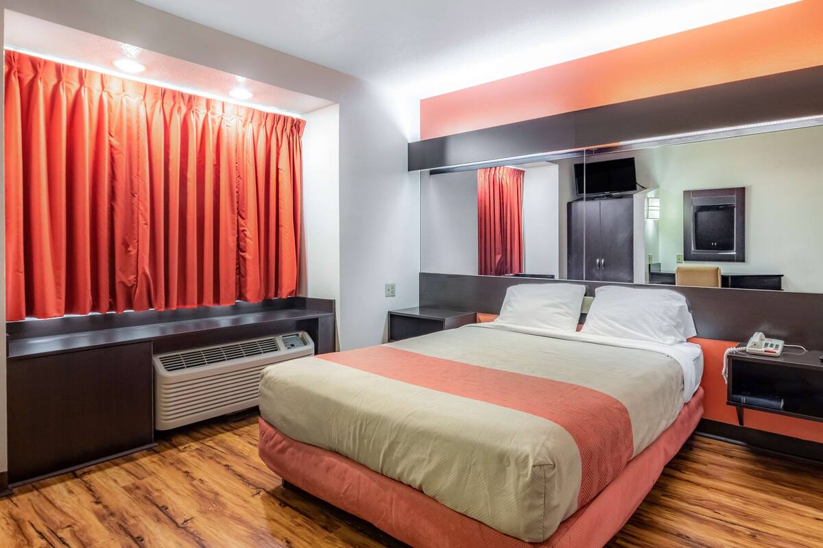 Une chambre d’hôtel avec un grand lit, une table de chevet avec un téléphone, un miroir et un téléviseur posé sur un meuble.