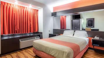 A hotel room with a large bed, a bedside table with a phone, a mirror, and a TV on a cabinet.