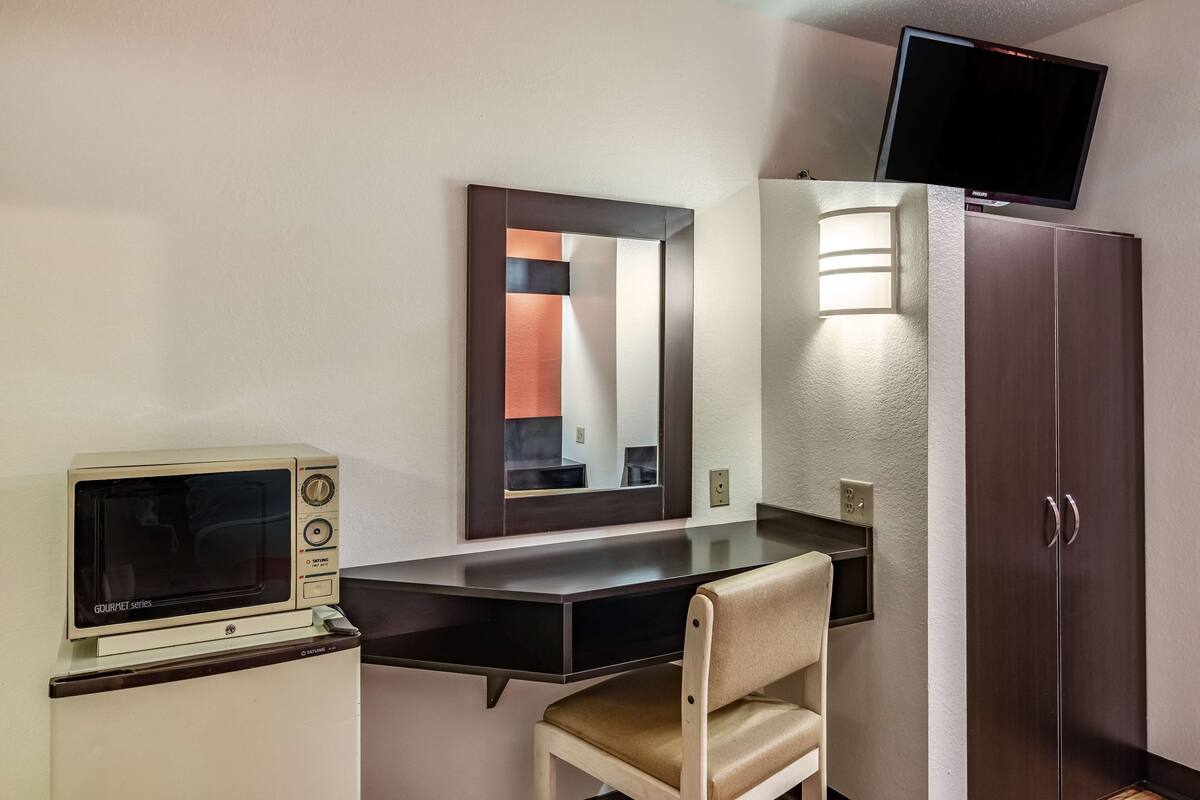 Une chambre d’hôtel équipée d’une kitchenette, d’un bureau avec une chaise, d’un miroir, d’un téléviseur fixé au mur et d’une armoire.