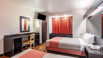 Une chambre d’hôtel équipée d’un bureau, d’une chaise, d’un lit, d’une télévision et d’une fenêtre avec des rideaux.