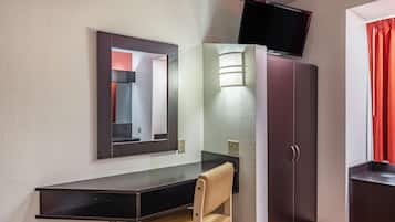 A room with a desk, chair, wardrobe, and a TV mounted on the wall.