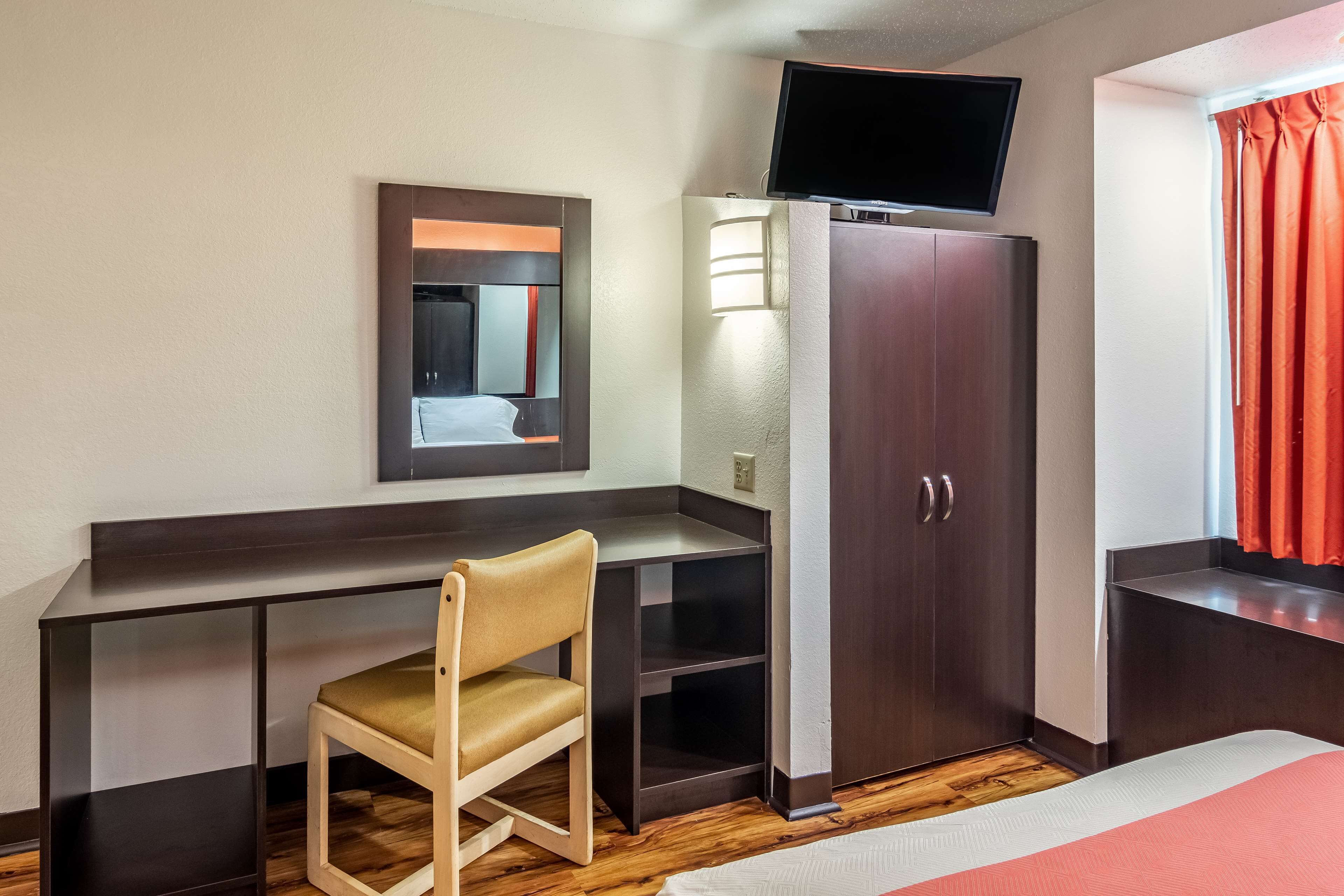 Une chambre d’hôtel comprenant un lit, un bureau avec une chaise, une armoire, un téléviseur fixé au mur et une fenêtre avec des rideaux.
