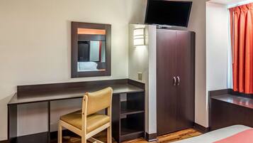 Une chambre d’hôtel comprenant un lit, un bureau avec une chaise, une armoire, un téléviseur fixé au mur et une fenêtre avec des rideaux.