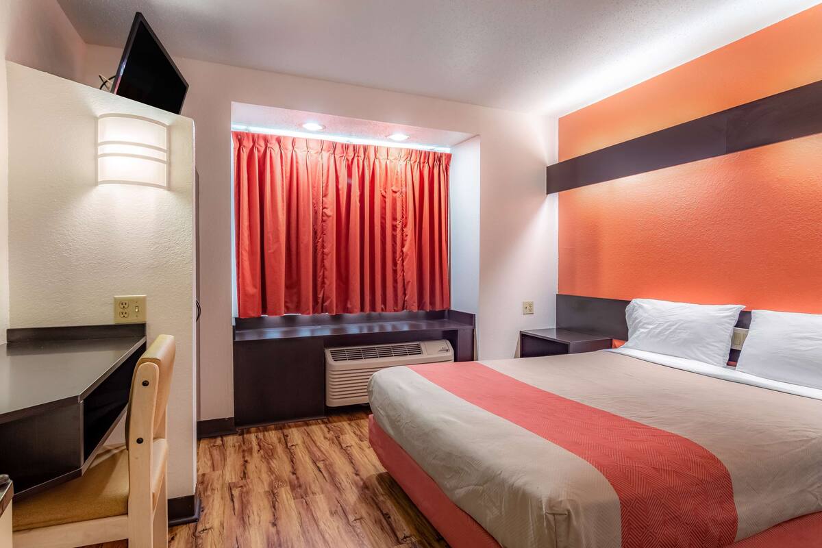 Une chambre d’hôtel équipée d’un lit, d’un bureau, d’une chaise, d’une télévision et d’une fenêtre avec des rideaux.