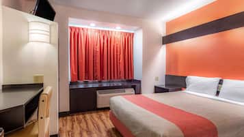 A hotel room with a bed, a desk, a chair, a TV, and a window with curtains.