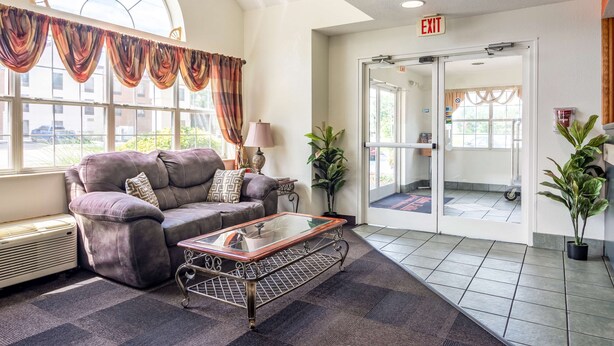 A lobby with a sofa, a glass-top coffee table, a lamp, and potted plants. - Motel 6 Chattanooga, TN - Downtown (Chattanooga)