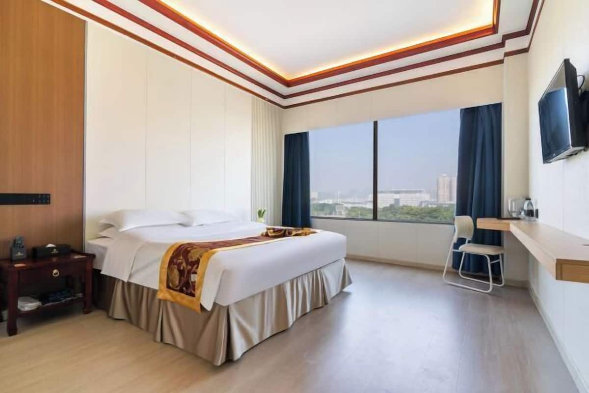 A hotel room with a bed, a desk, a TV, and a large window with a city view.
