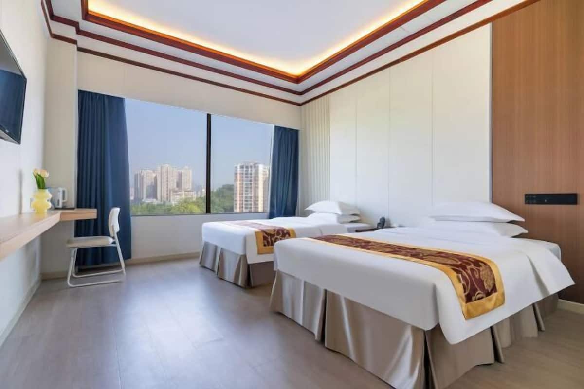 A hotel room with two beds, a desk, a chair, and a large window with a city view.