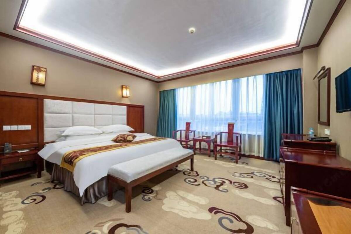 A hotel room with a large bed, a desk, a chair, a small table, and a window with curtains.