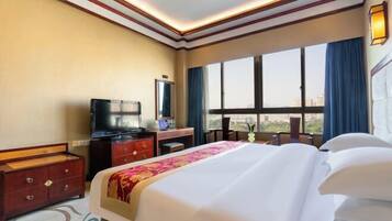 A hotel room with a large bed, a desk with a television, and a window with curtains.
