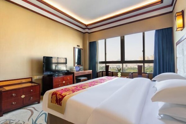 A hotel room with a large bed, a desk with a television, and a window with curtains.