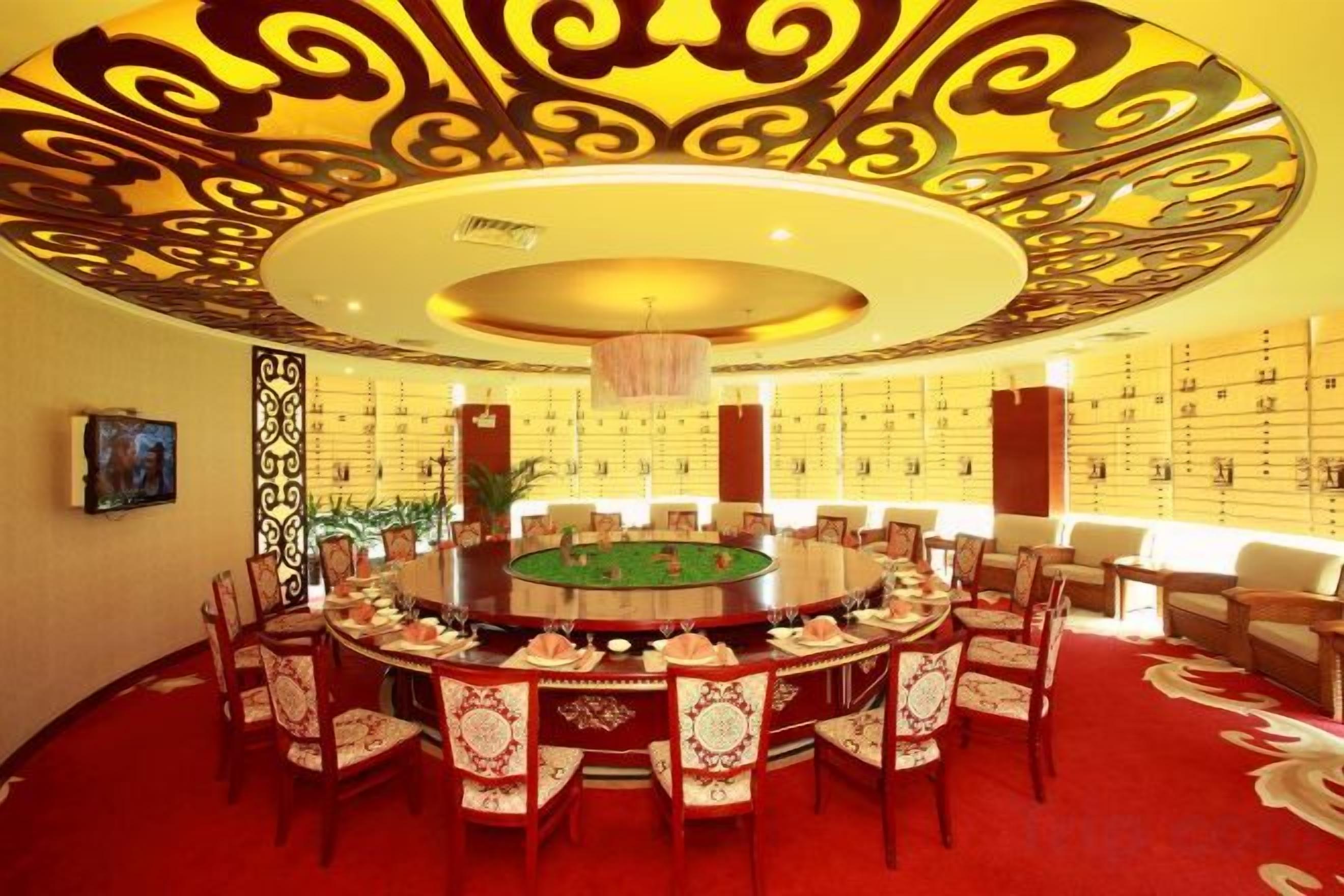 A round dining table surrounded by chairs, a chandelier, and a patterned ceiling.