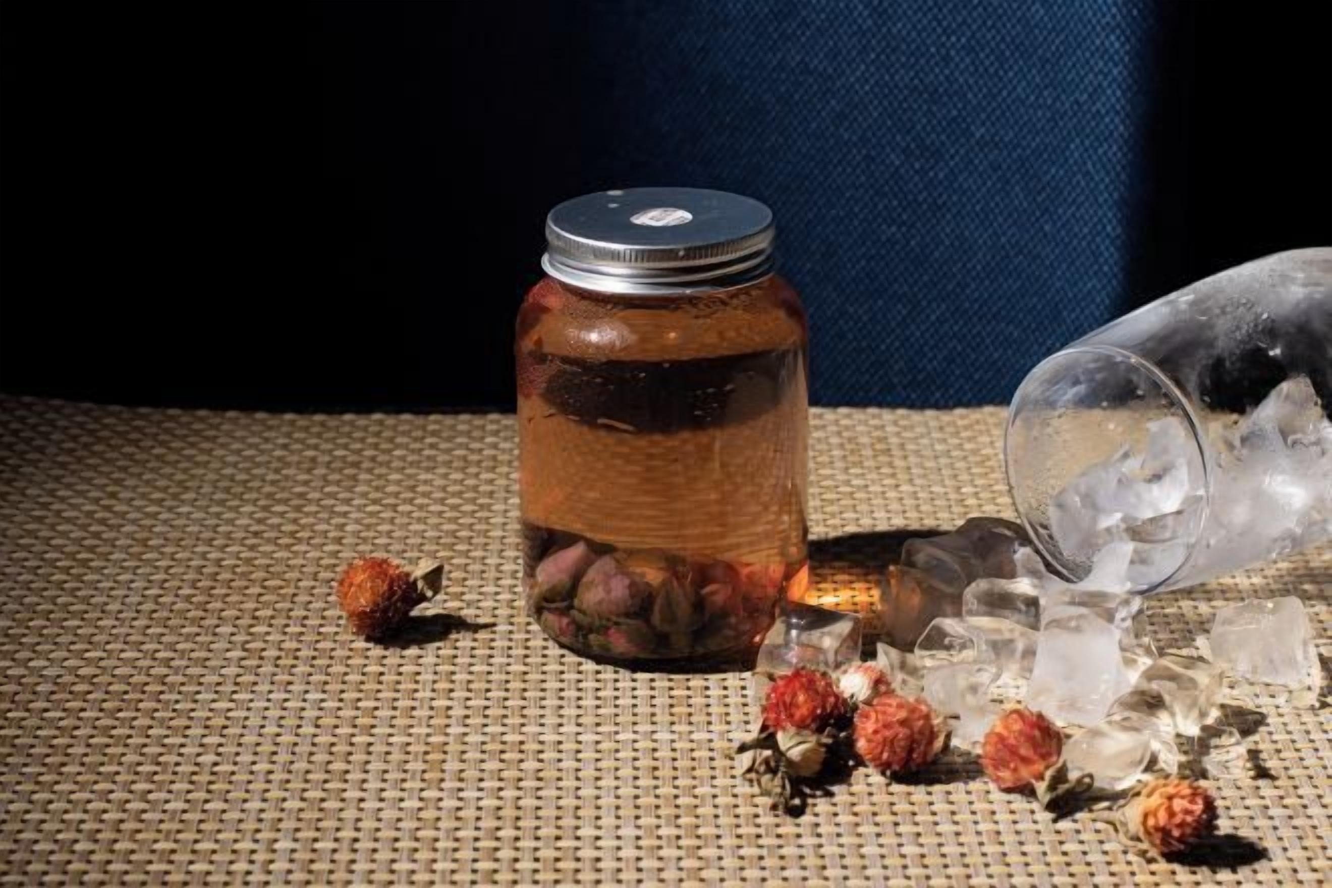 A jar with a metal lid, ice cubes, and scattered berries on a textured surface.