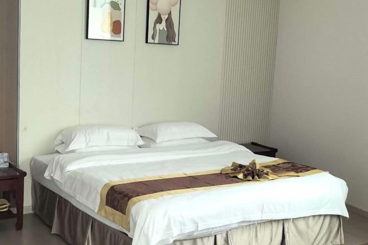 A neatly made bed with a white duvet and a brown throw, a bedside table with a lamp, and two framed pictures on the wall.