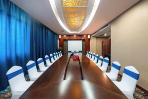 A conference room with a long table, white chairs with blue sashes, a projector screen, and a blue curtain backdrop. - Pingguo International Hotel (Pingguo)