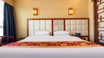A hotel room with a large bed, two wall sconces, a wooden headboard, and a decorative bed runner.