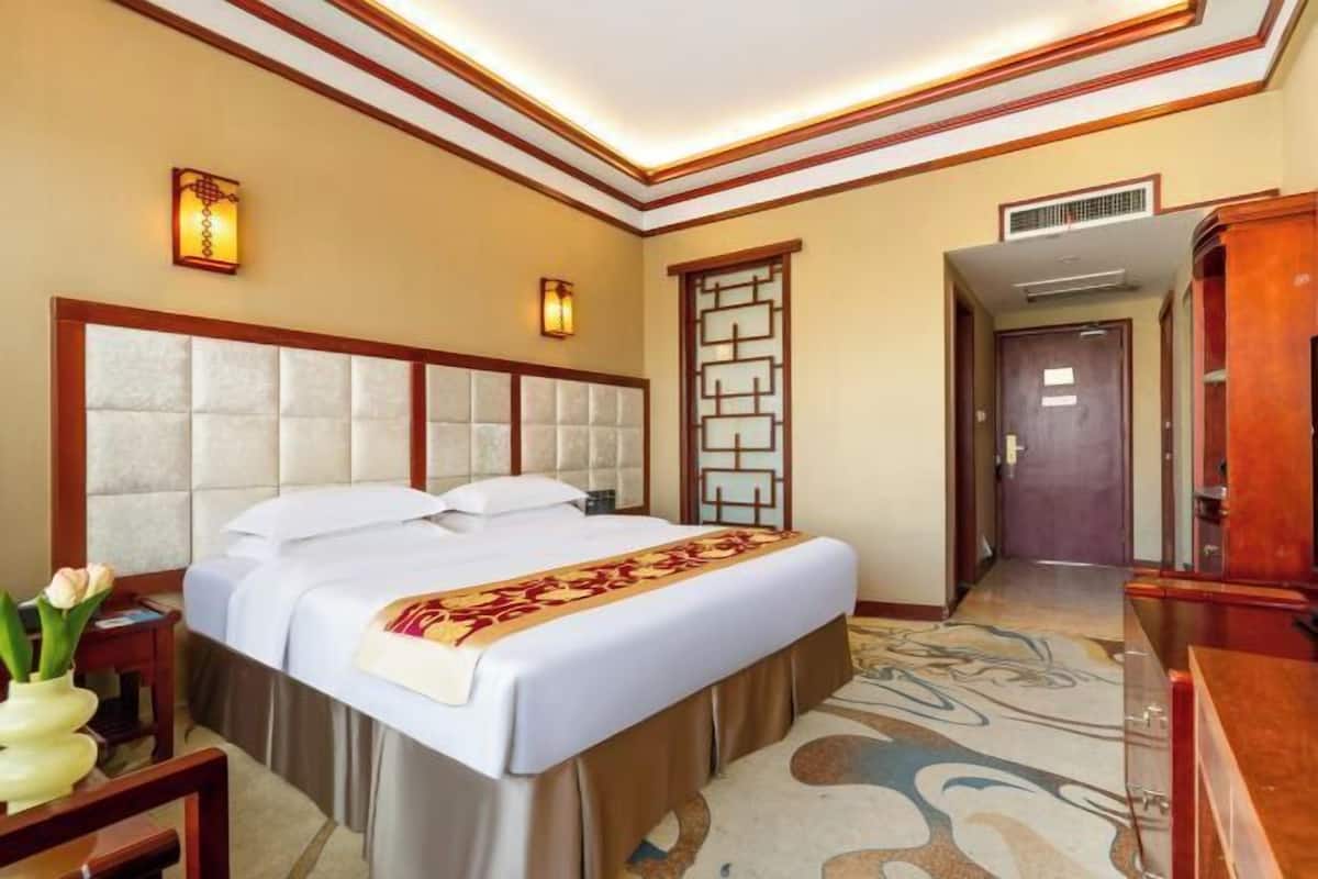A hotel room with a large bed, a bedside table, a nightstand, a decorative wall panel, and a carpeted floor.