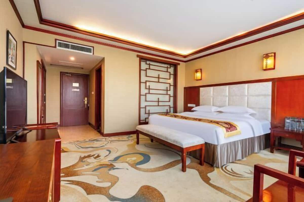 A hotel room with a bed, a desk, a chair, a TV, and a decorative wall panel.